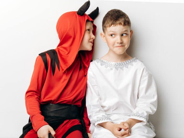 Dos niños con disfraces de ángel y demonio sobre fondo blanco